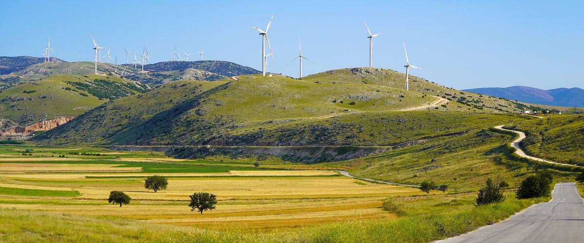 A winding road through a hilly landscape with wind turbines in the distance.