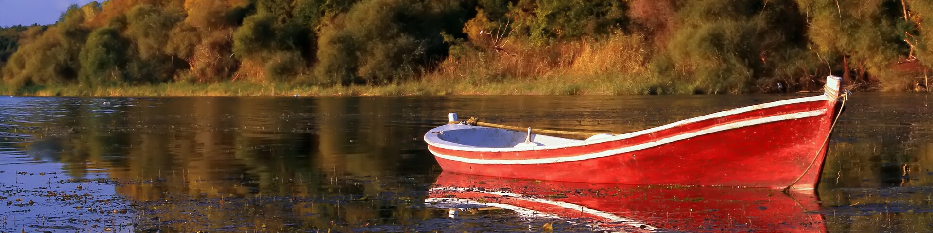 Um barco vermelho com listras brancas em águas calmas, rodeado por árvores com folhagem de outono.