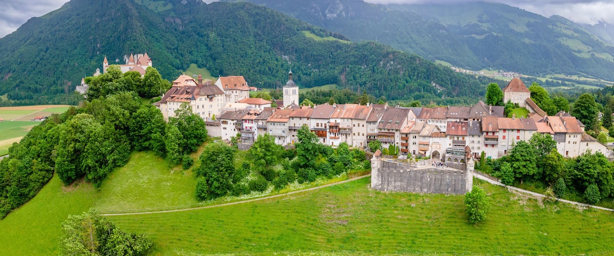 A historic town with a castle on a hill, surrounded by lush green fields and mountains.