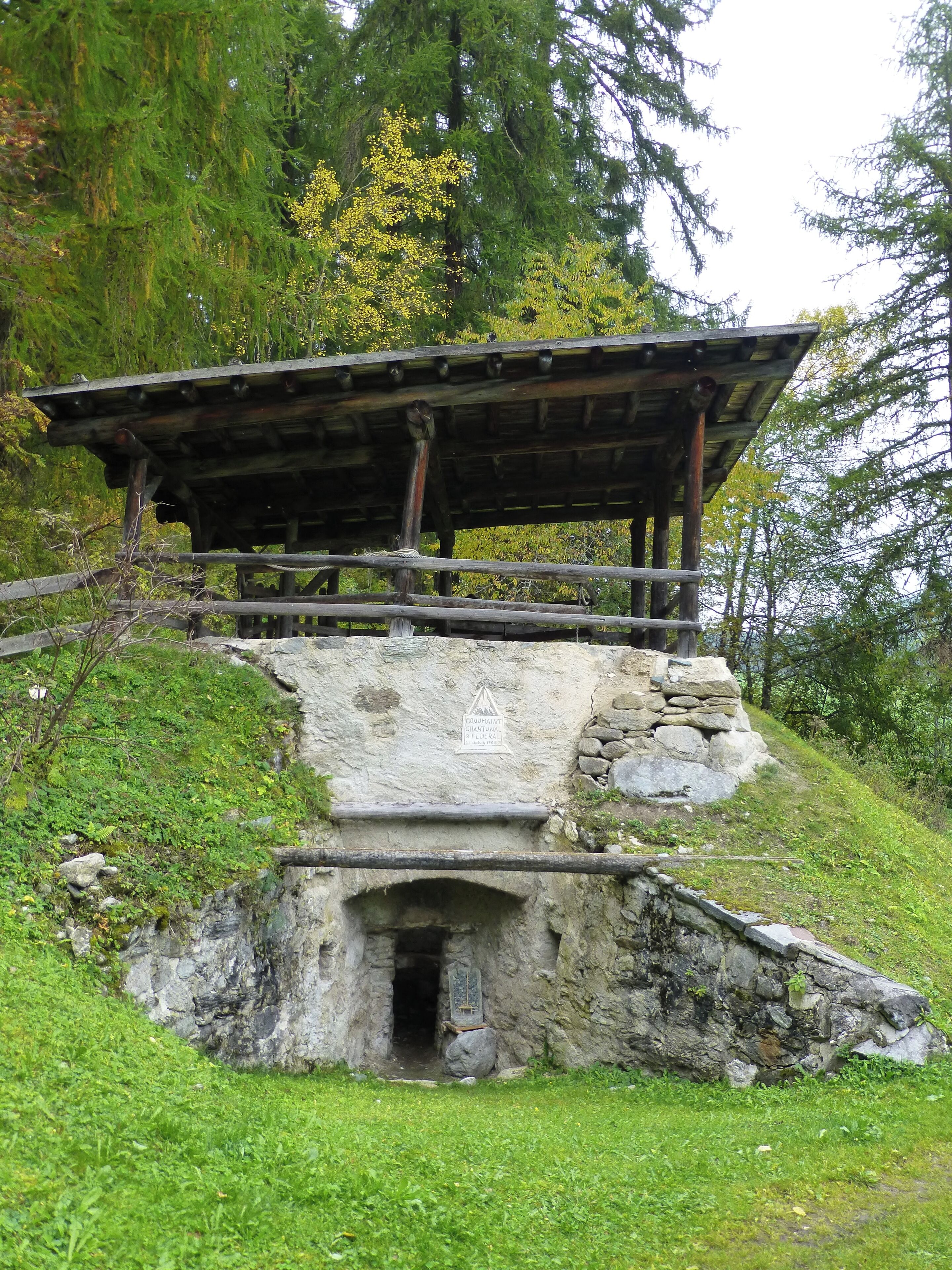 A stone structure with a wooden roof, surrounded by greenery and trees.