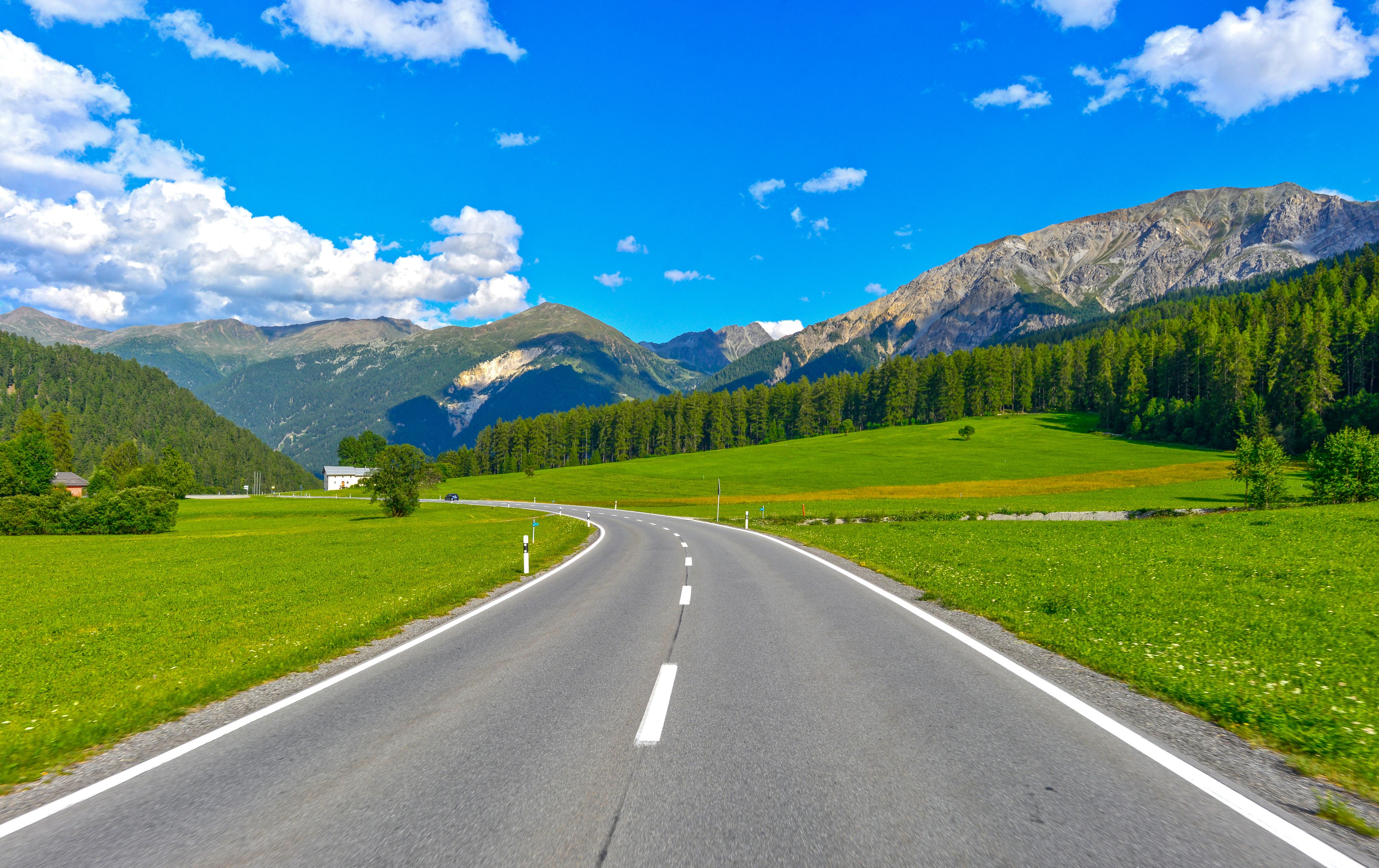 A road curving through a green valley with mountains in the background.