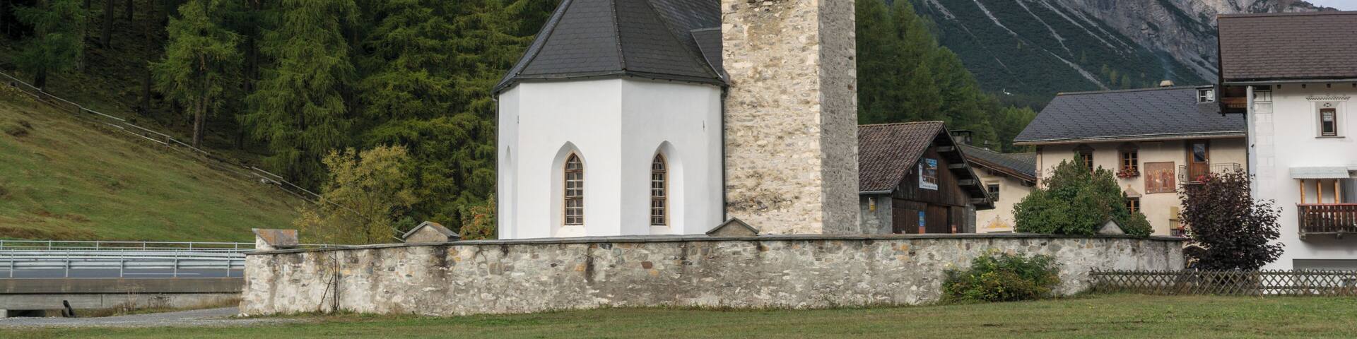 A church with a clock tower, surrounded by mountains and trees.