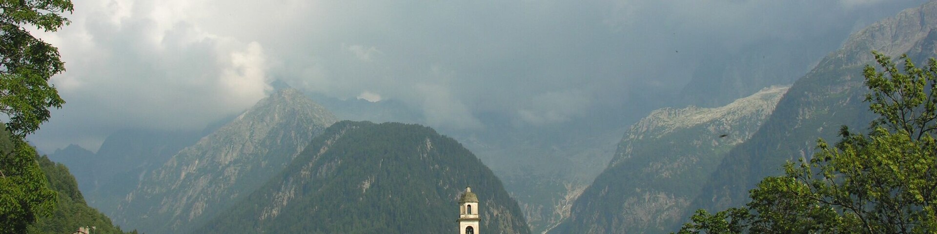 Un paisaje montañoso con una torre de iglesia, casas y abundante vegetación.