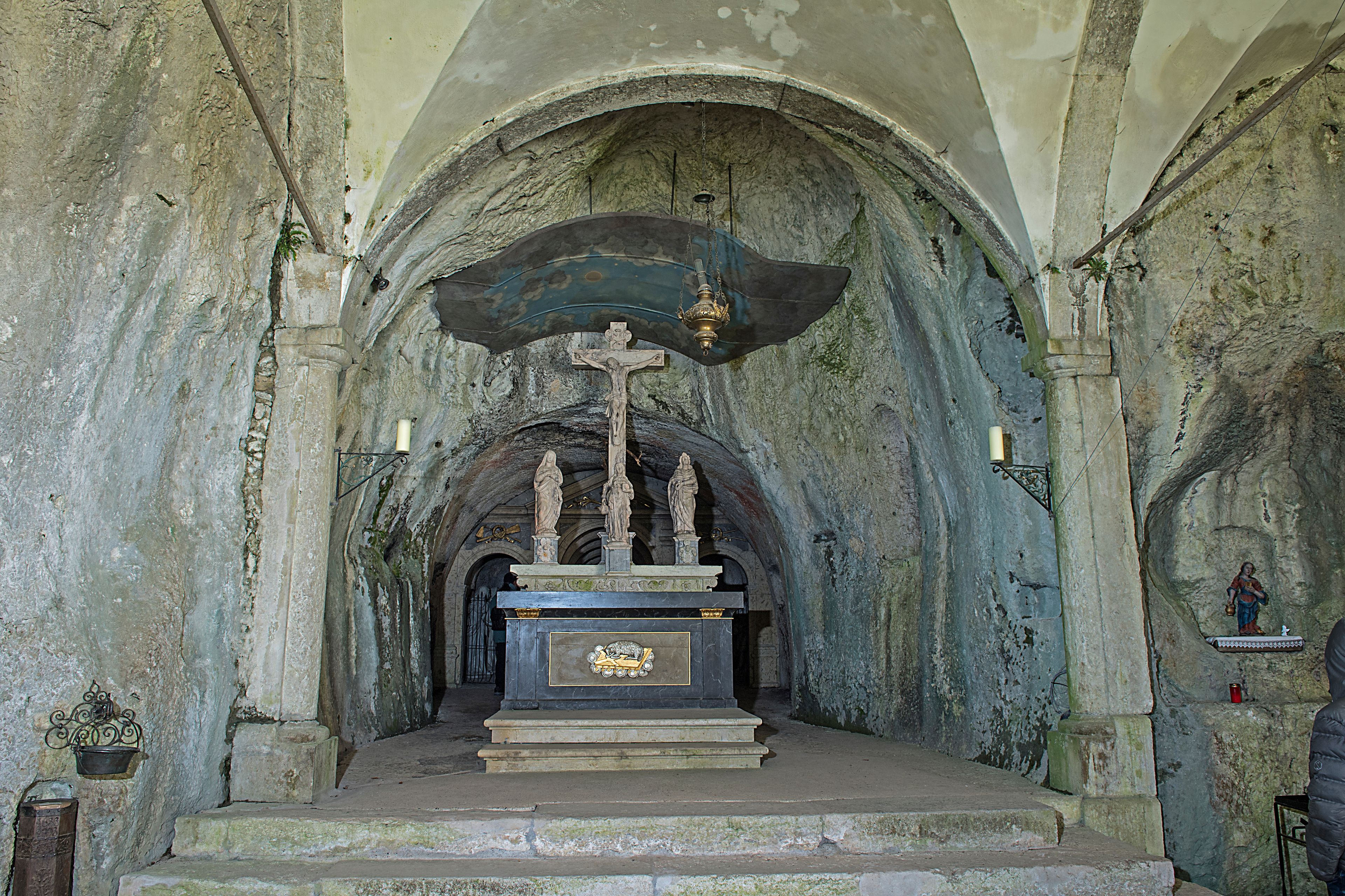 An ancient church interior with a crucifix, stone arches, and a statue of the Virgin Mary.