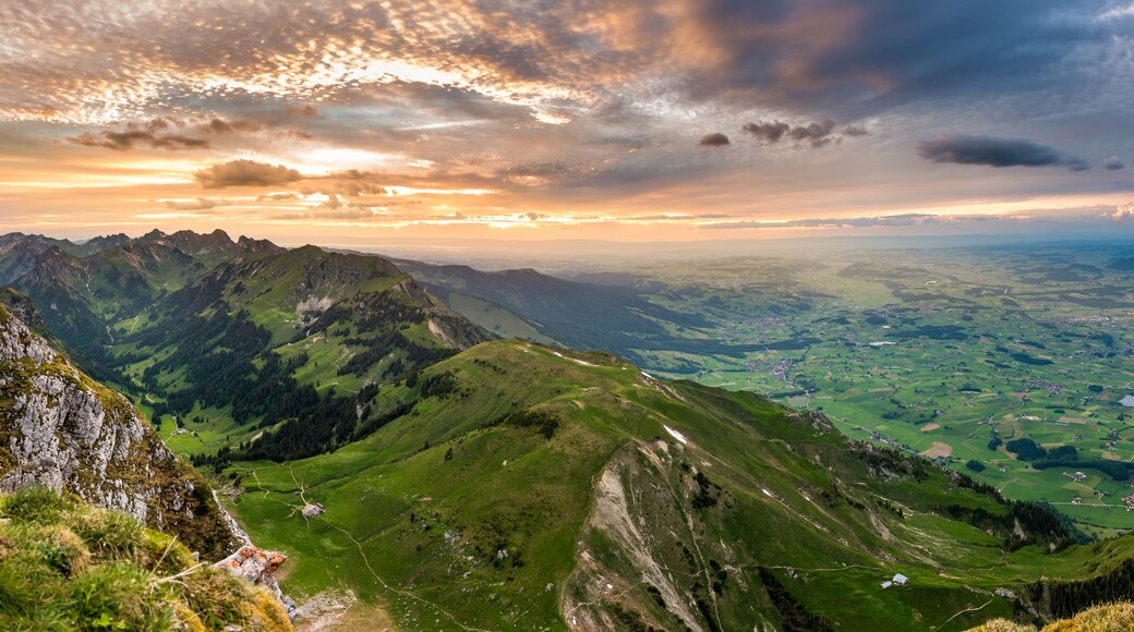 Een bergachtig landschap met groene valleien en een stad in de verte.