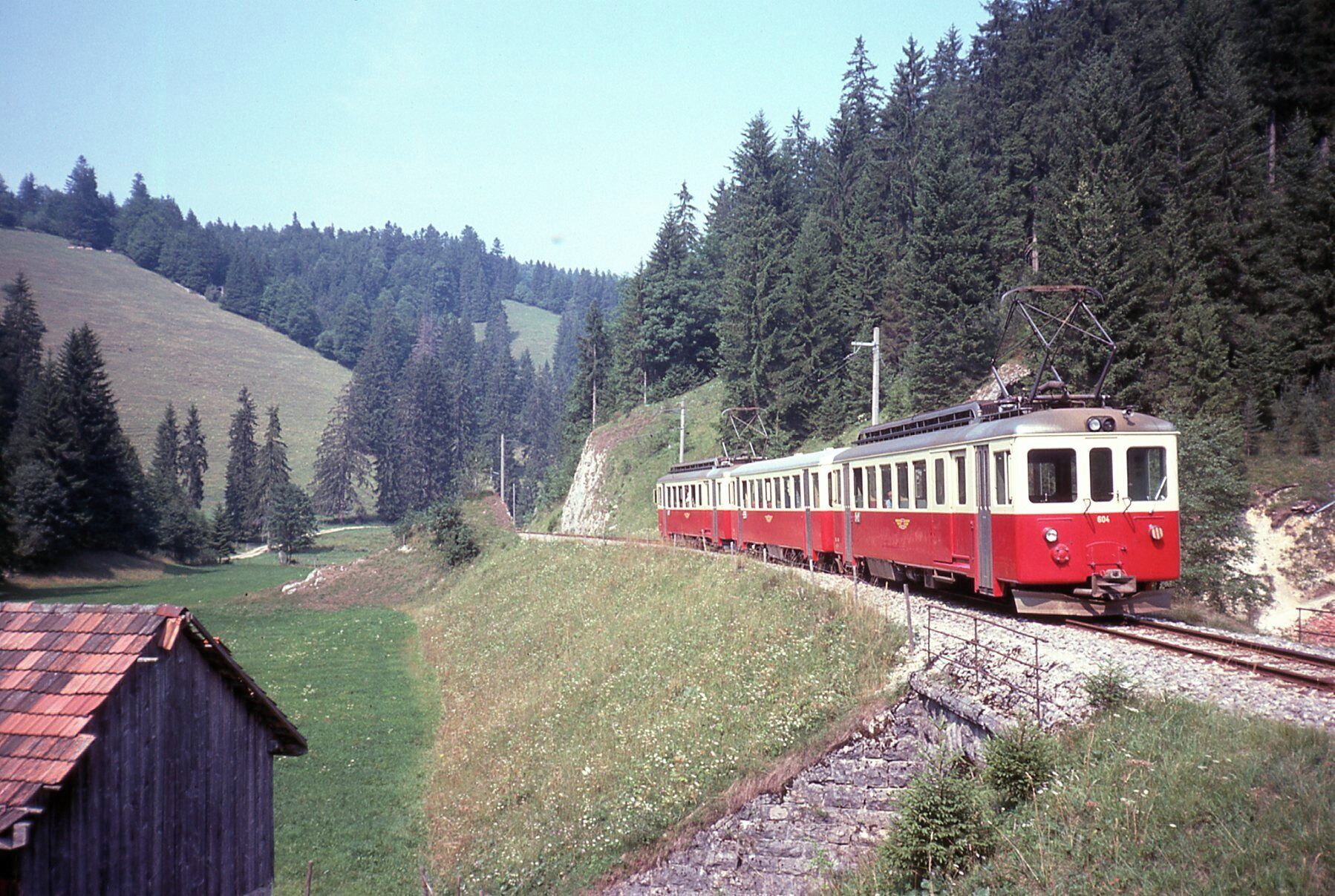 A red and white train traveling through a forested area with a small building on the left.