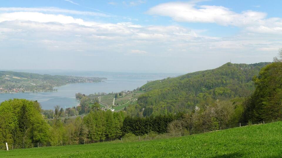 A lake surrounded by hills, a town in the distance, and a clear sky.