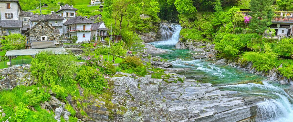 A mountainous village with stone houses, a flowing river, and lush greenery.