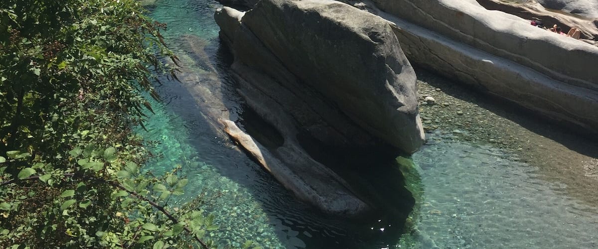A clear river with large rocks and lush greenery in a mountainous area.