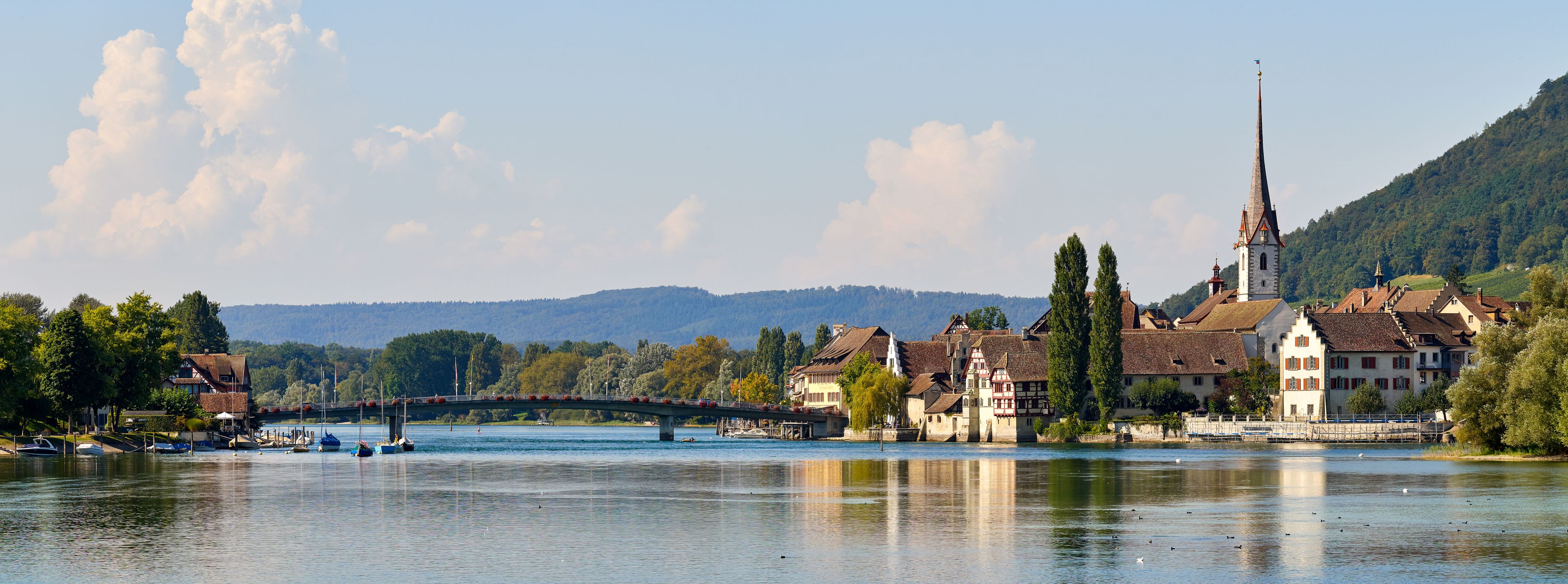 A riverside town with a bridge, historic buildings, and a church with a tall spire.
