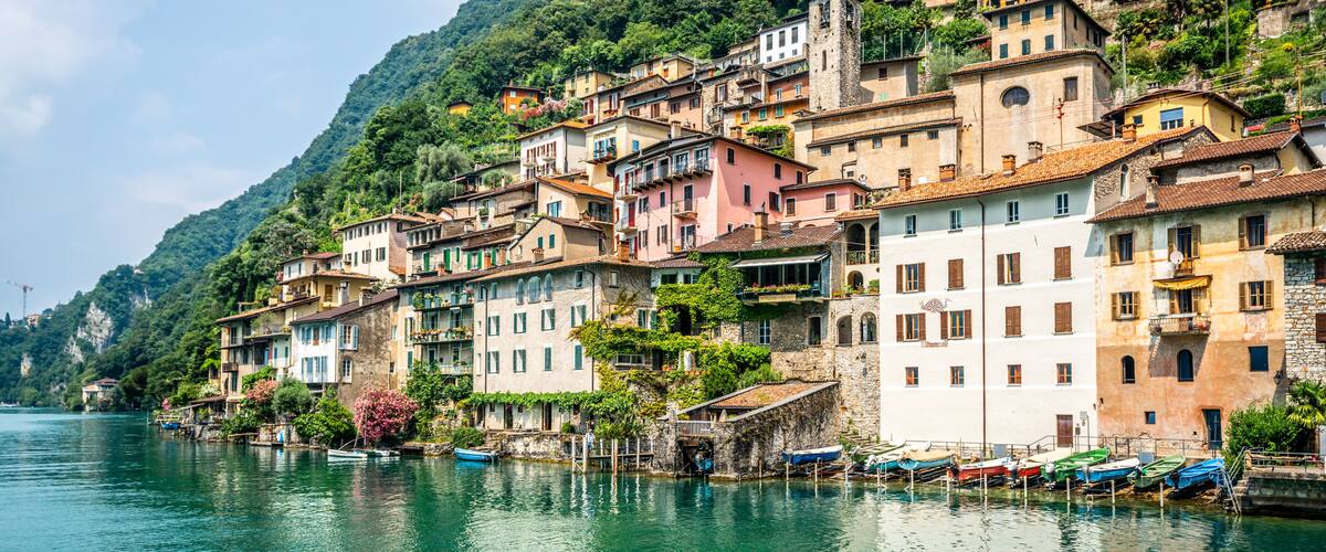 A hillside village with colorful buildings, a calm lake, and boats docked along the shore.