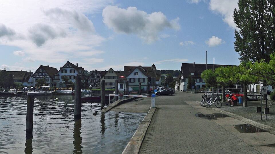 A riverside town with historic buildings, a dock with boats, and a row of red canoes.