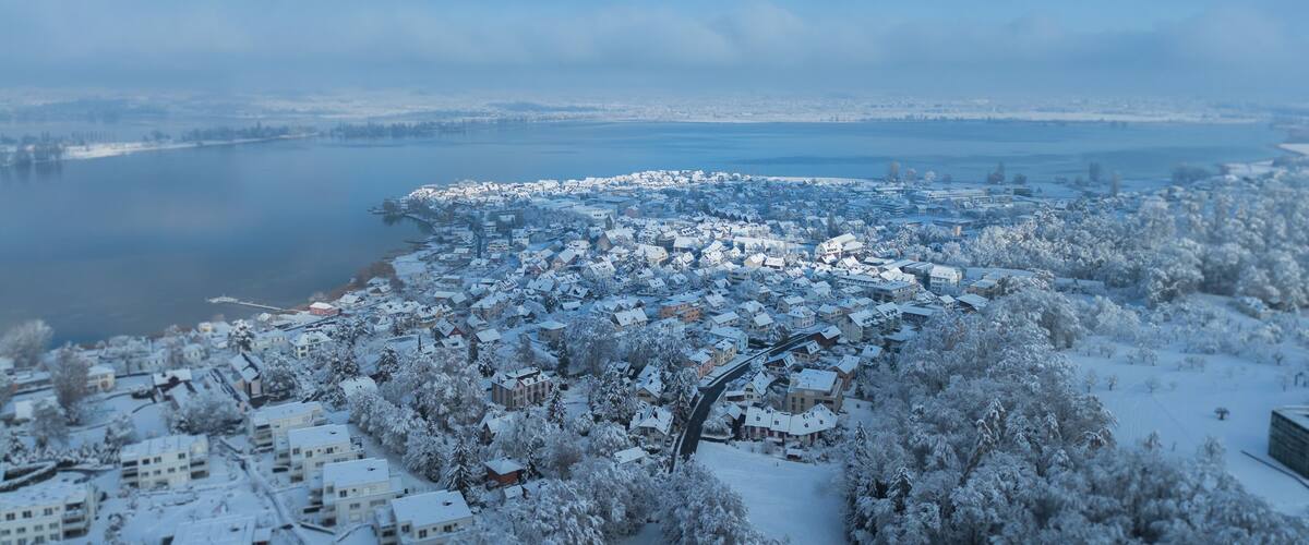 A snow-covered town by a lake with a mix of residential and commercial buildings.