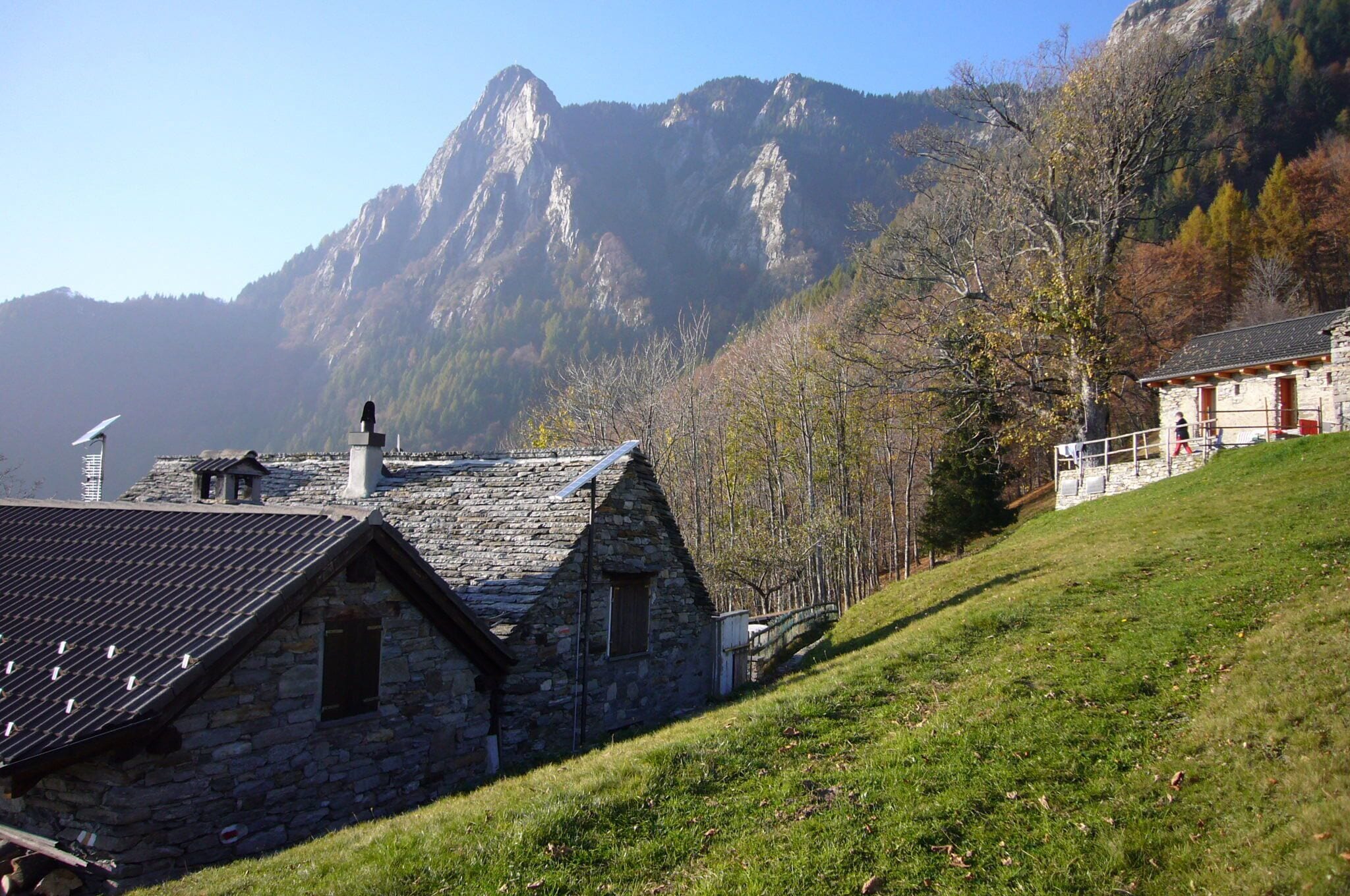 A stone house with a sloped roof, a mountain in the background, and a grassy hillside.