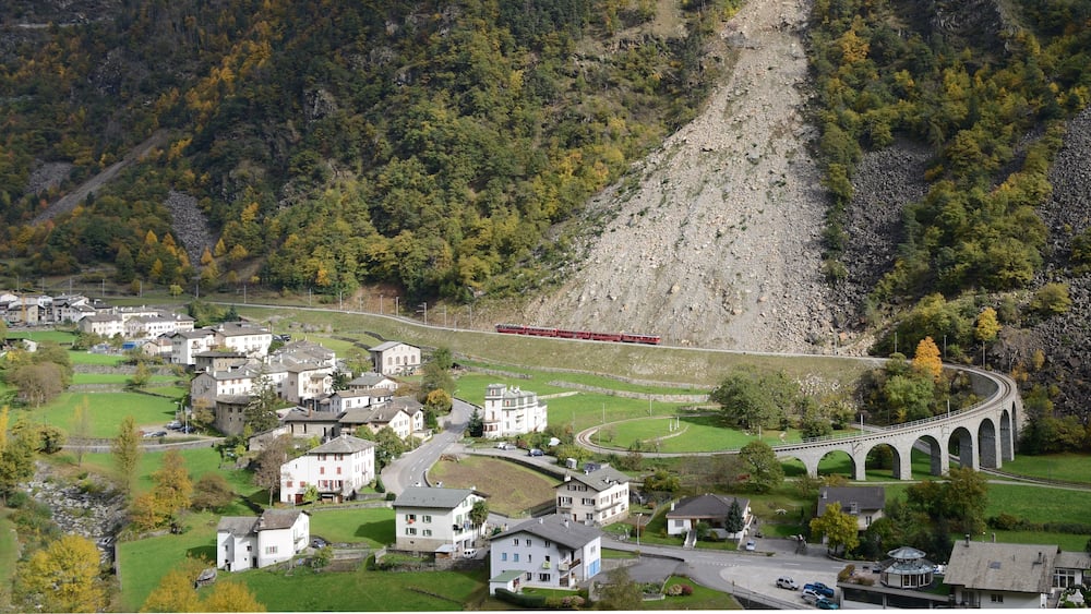 Une voie ferrée pittoresque, avec un viaduc en pierre, entourée d’un village aux maisons et à la végétation luxuriante.
