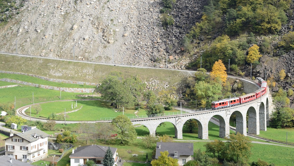 Ein roter Zug auf einer gewölbten Steinbrücke über einem Tal.