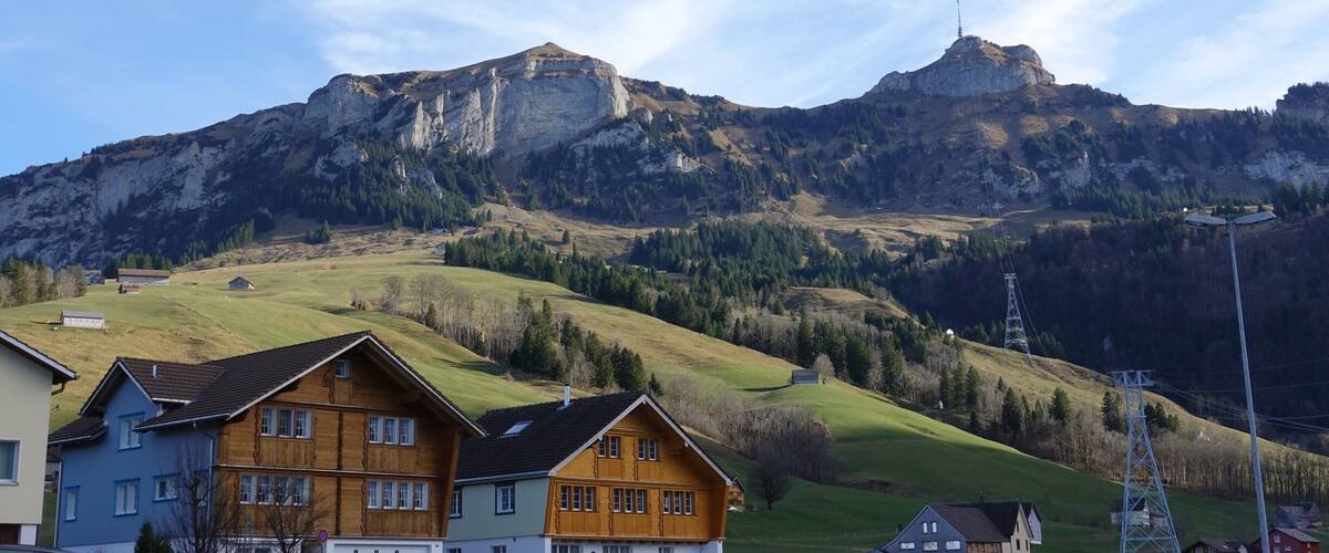 A mountain with a prominent peak, a valley with houses, and a clear sky.