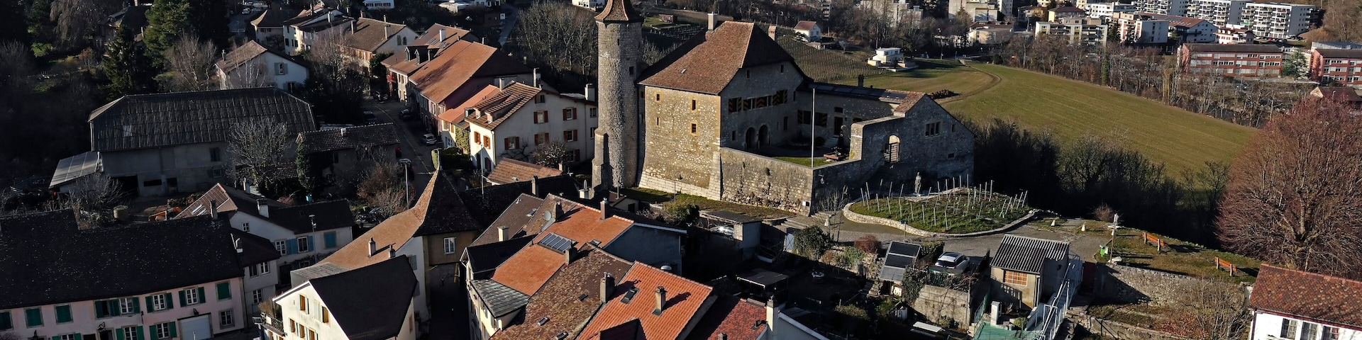 Uma cidade com edifícios históricos, uma torre imponente e uma ponte ao fundo.