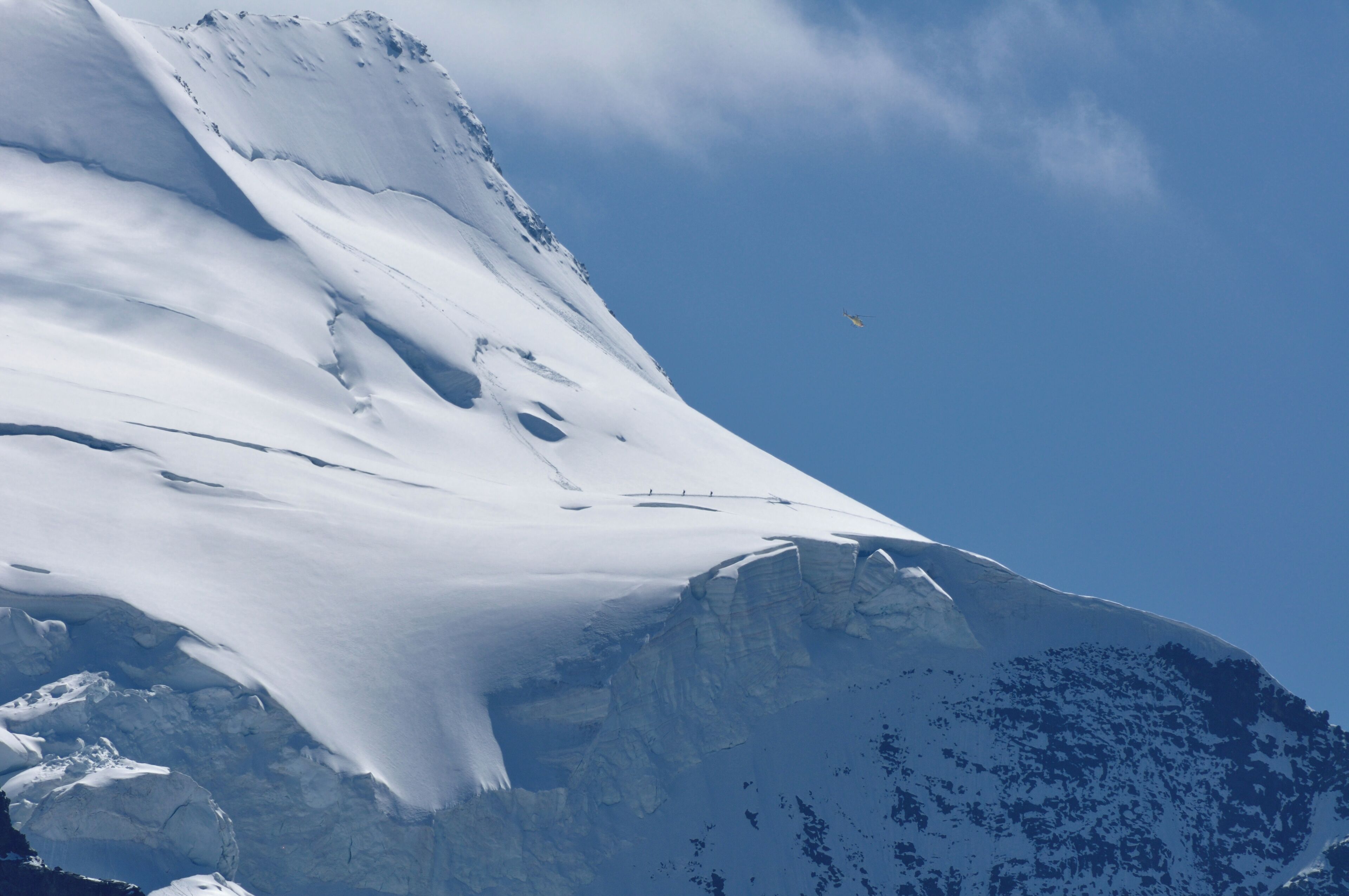 Switzerland, Graubünden, a Heli Bernina Eurocopter AS 350 overhead 3 mountaineers below Bellavista, seen from Diavolezza.