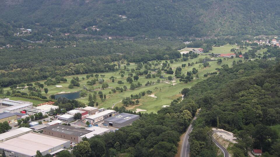A golf course surrounded by dense forest and industrial buildings.