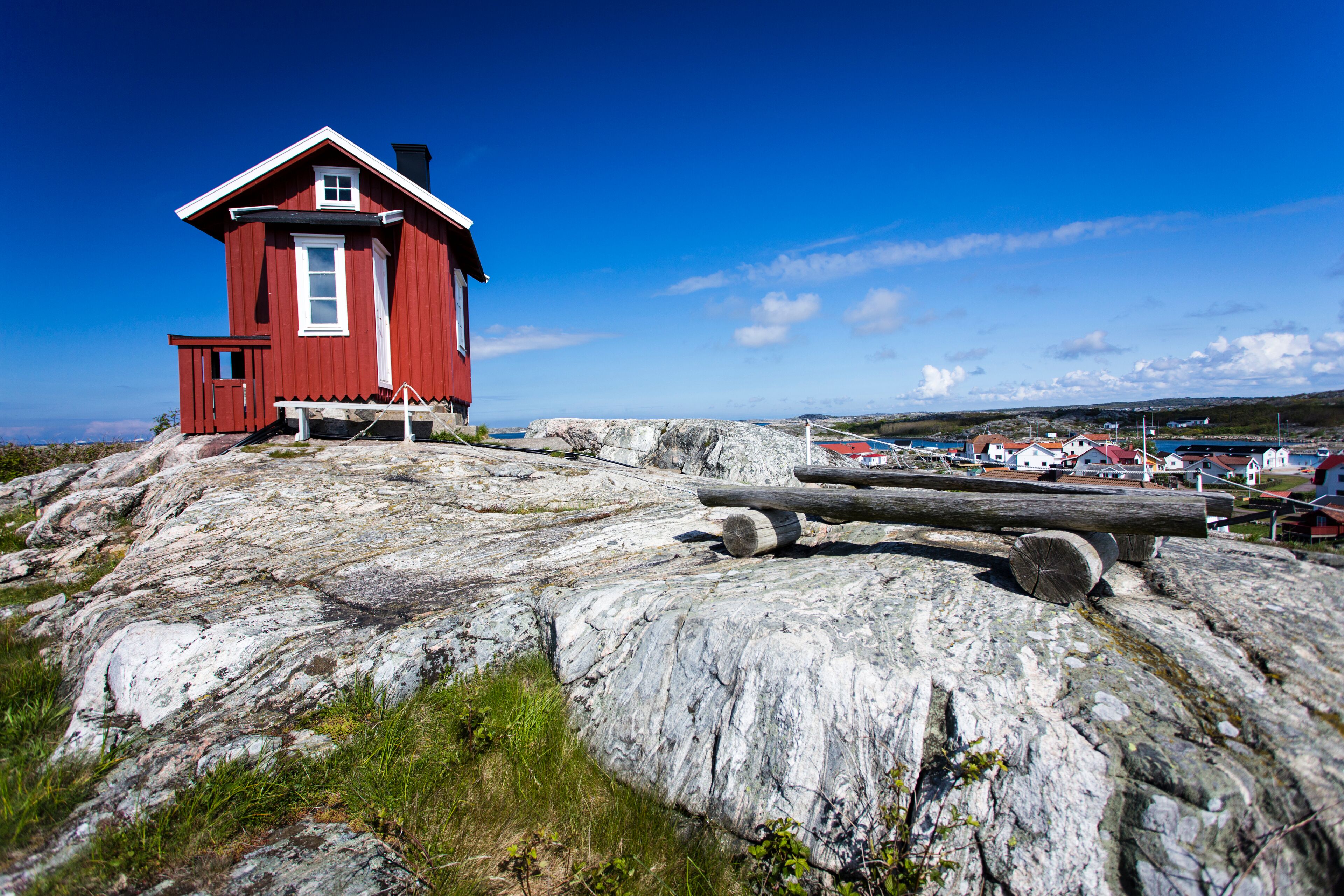 A red wooden house on a rocky outcrop with a clear blue sky.