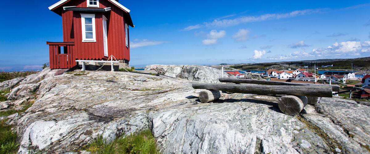 A red wooden house on a rocky outcrop with a clear blue sky.