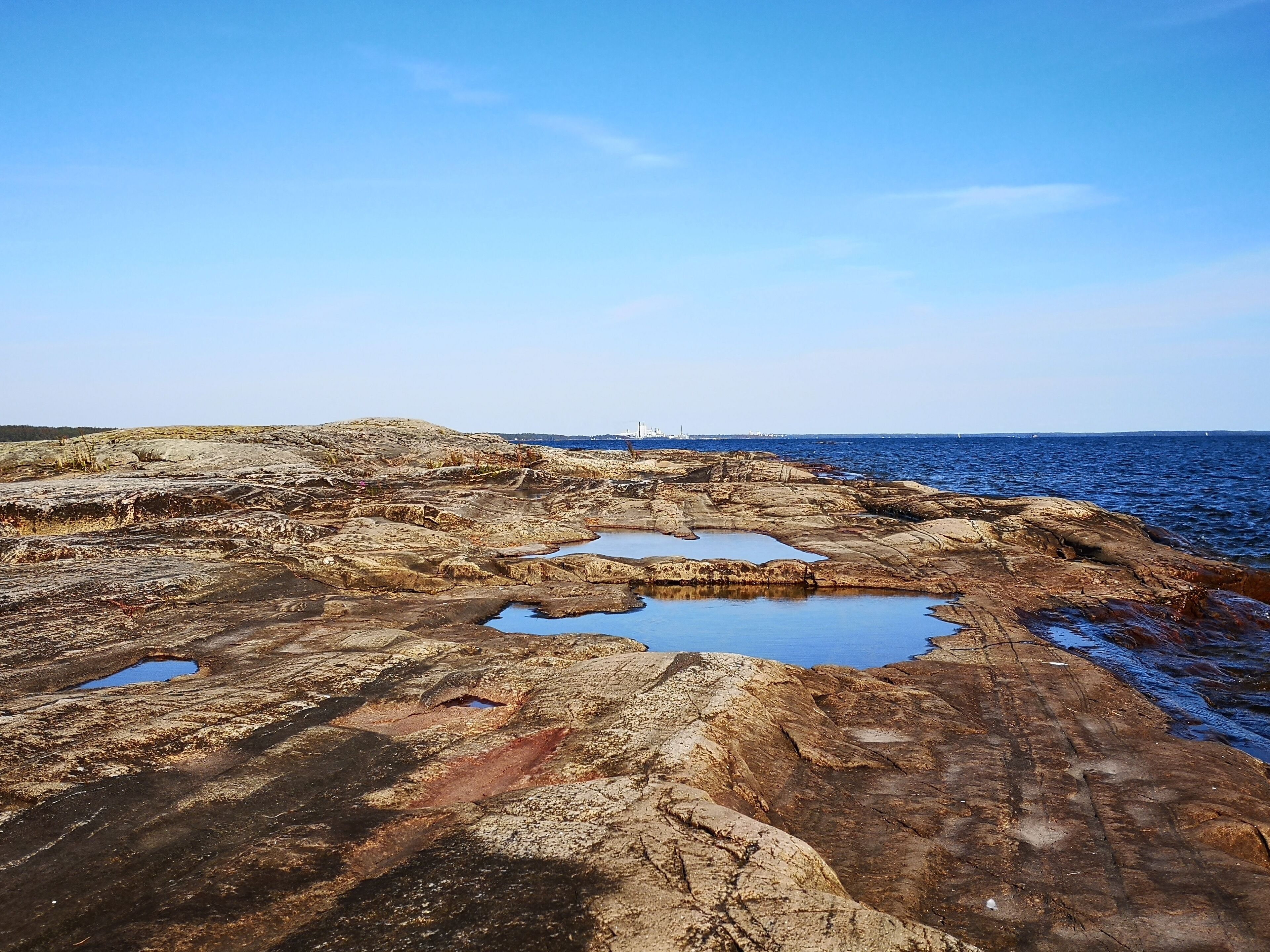 A rocky coastline with pools of water and a distant ship.