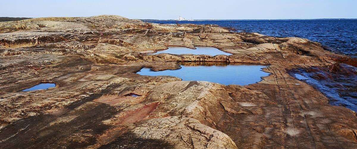 A rocky coastline with pools of water and a distant ship.