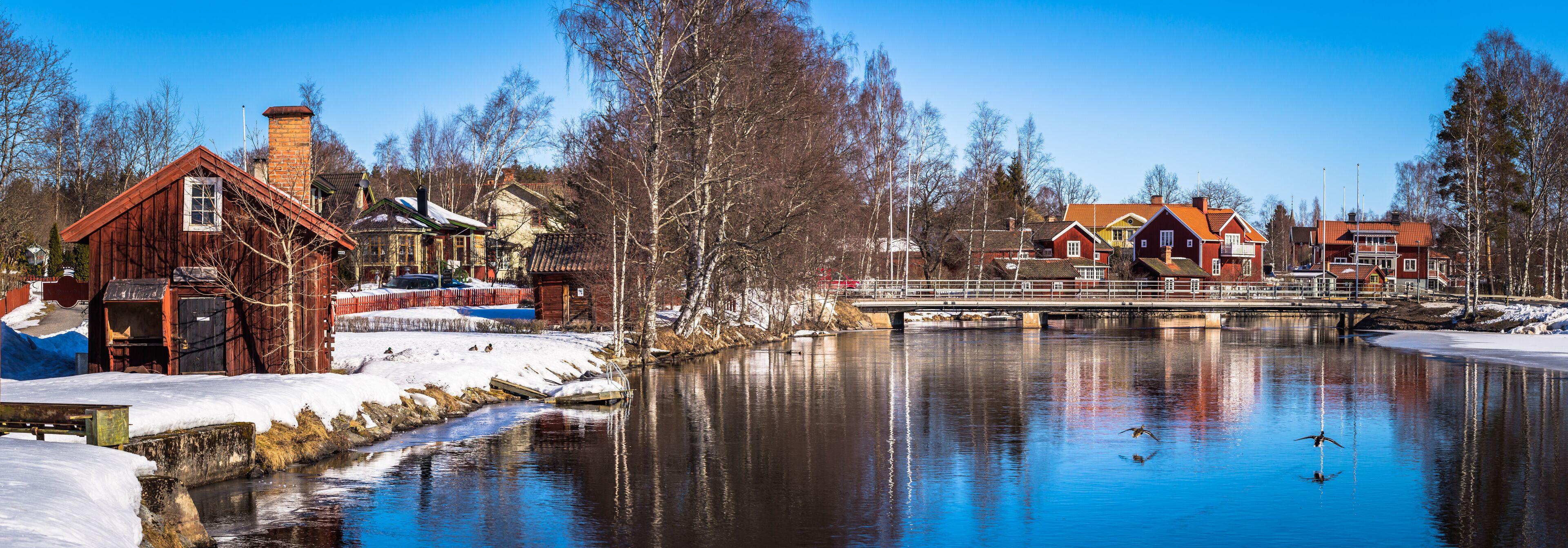 A riverside town with wooden buildings, a bridge, and snow-covered ground.