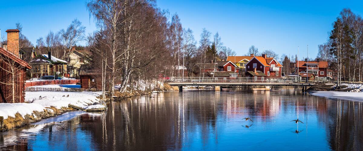 A riverside town with wooden buildings, a bridge, and snow-covered ground.