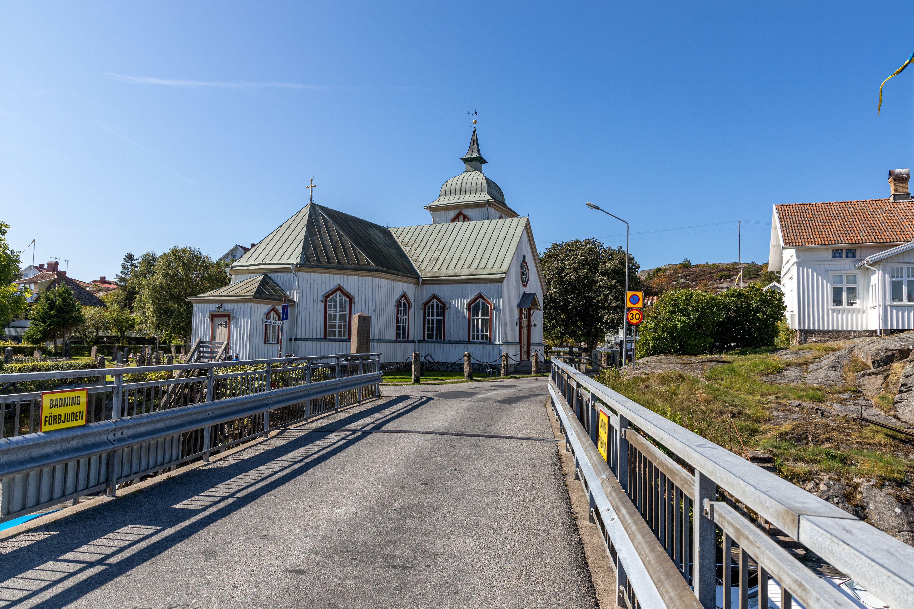 A white church with a green roof and a bell tower, surrounded by a gravel road and metal railings.