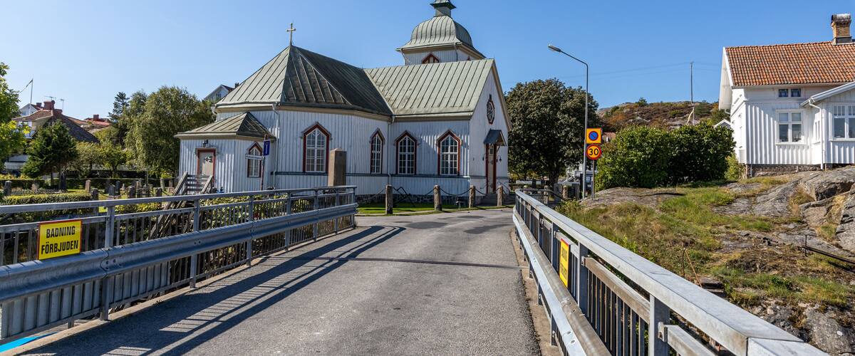 A white church with a green roof and a bell tower, surrounded by a gravel road and metal railings.
