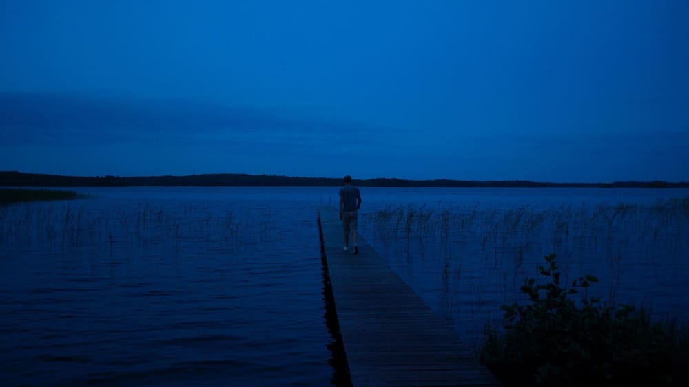 A person walking on a wooden pier extending into a body of water at dusk.