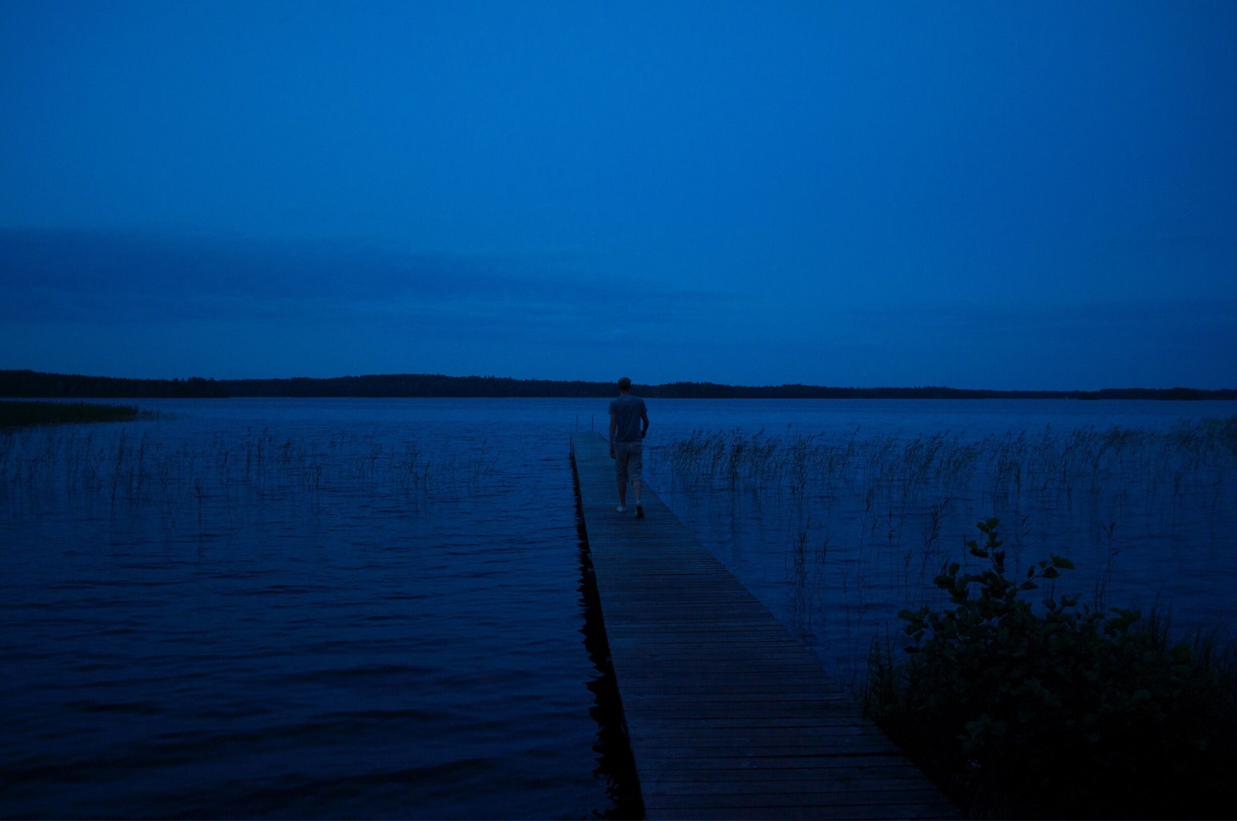 A person walking on a wooden pier extending into a body of water at dusk.