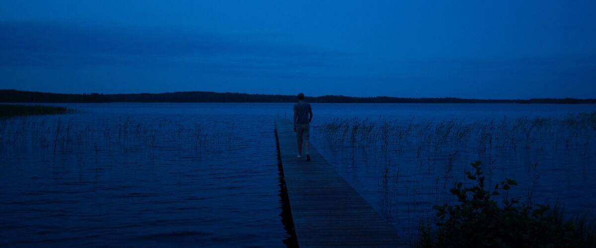 A person walking on a wooden pier extending into a body of water at dusk.