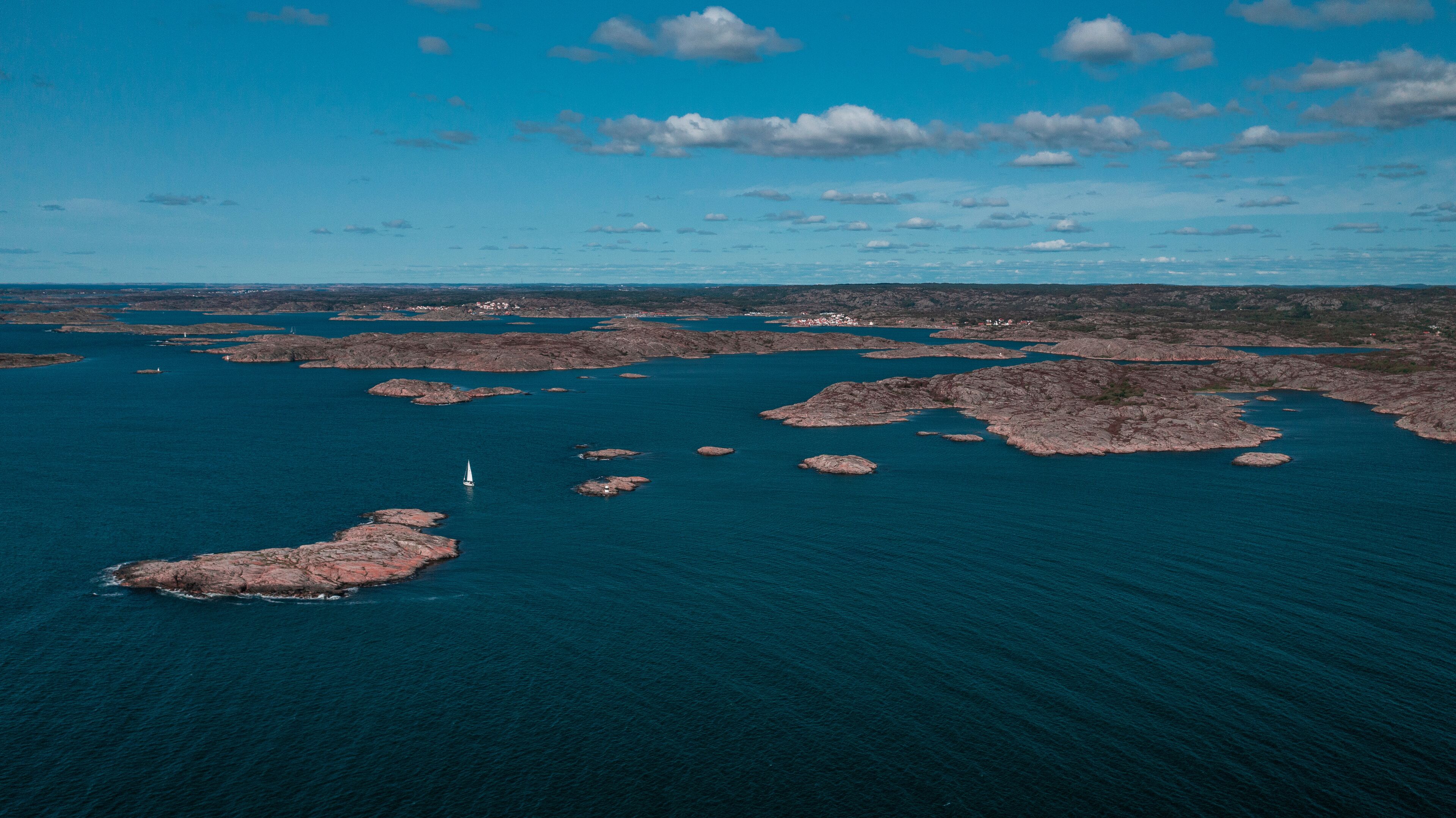 A coastal landscape with rocky outcrops and a sailboat in the water.