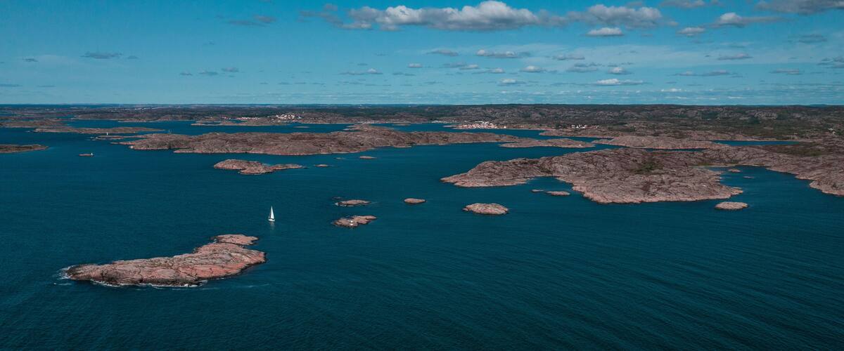 A coastal landscape with rocky outcrops and a sailboat in the water.