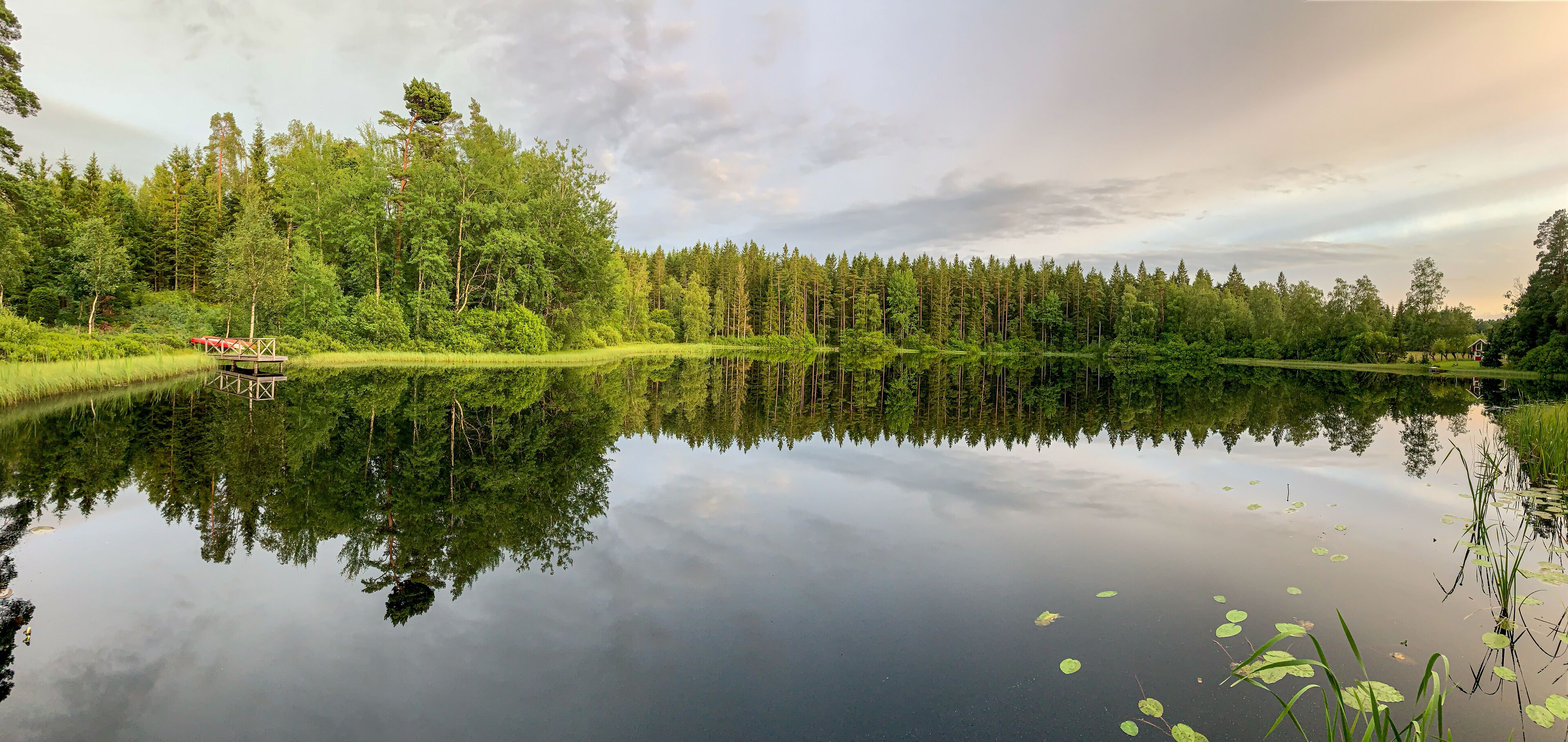 A calm lake surrounded by dense forest, a wooden dock, and a small house.