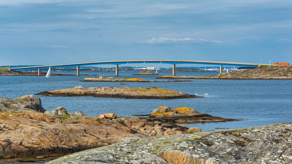 Un paysage côtier avec un pont, des rivages rocheux et un voilier.