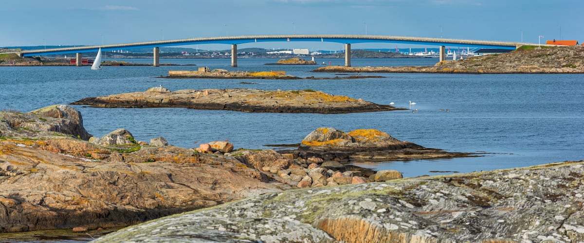 A coastal landscape with a bridge, rocky shores, and a sailboat.