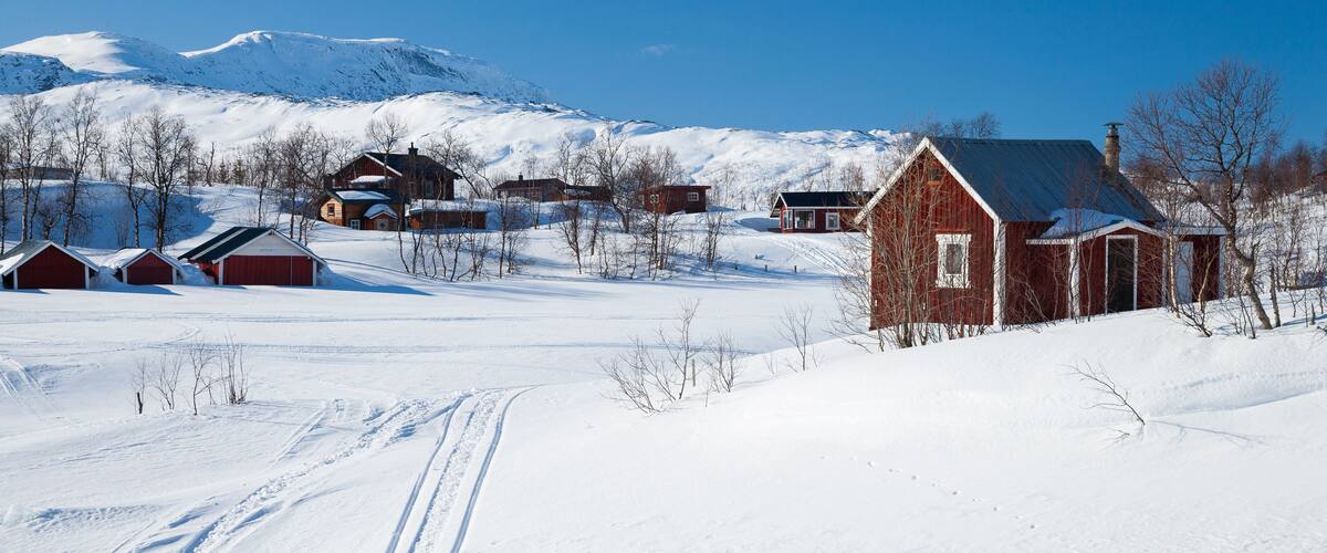 A snowy rural landscape with a red barn, houses, and a clear blue sky.