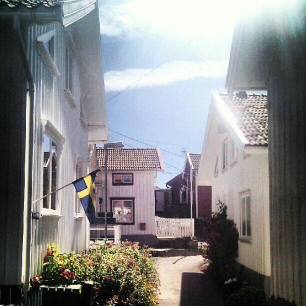 A narrow street with white houses, a Swedish flag, and a clear sky.