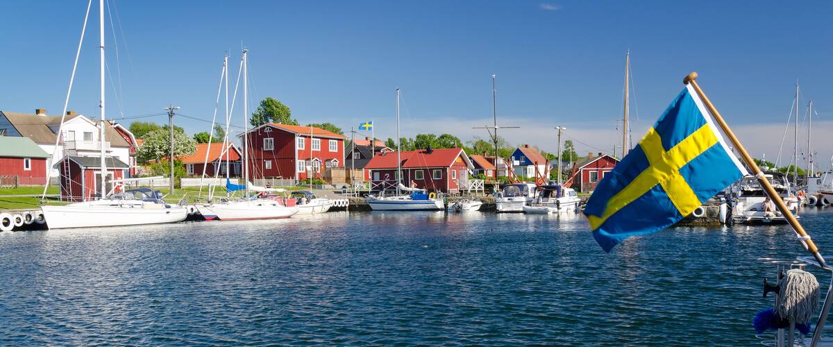 A marina with boats, a Swedish flag, and red houses along the water.