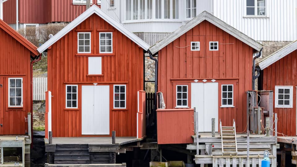 A row of red wooden houses with white doors and windows, wooden steps, and a dock.
