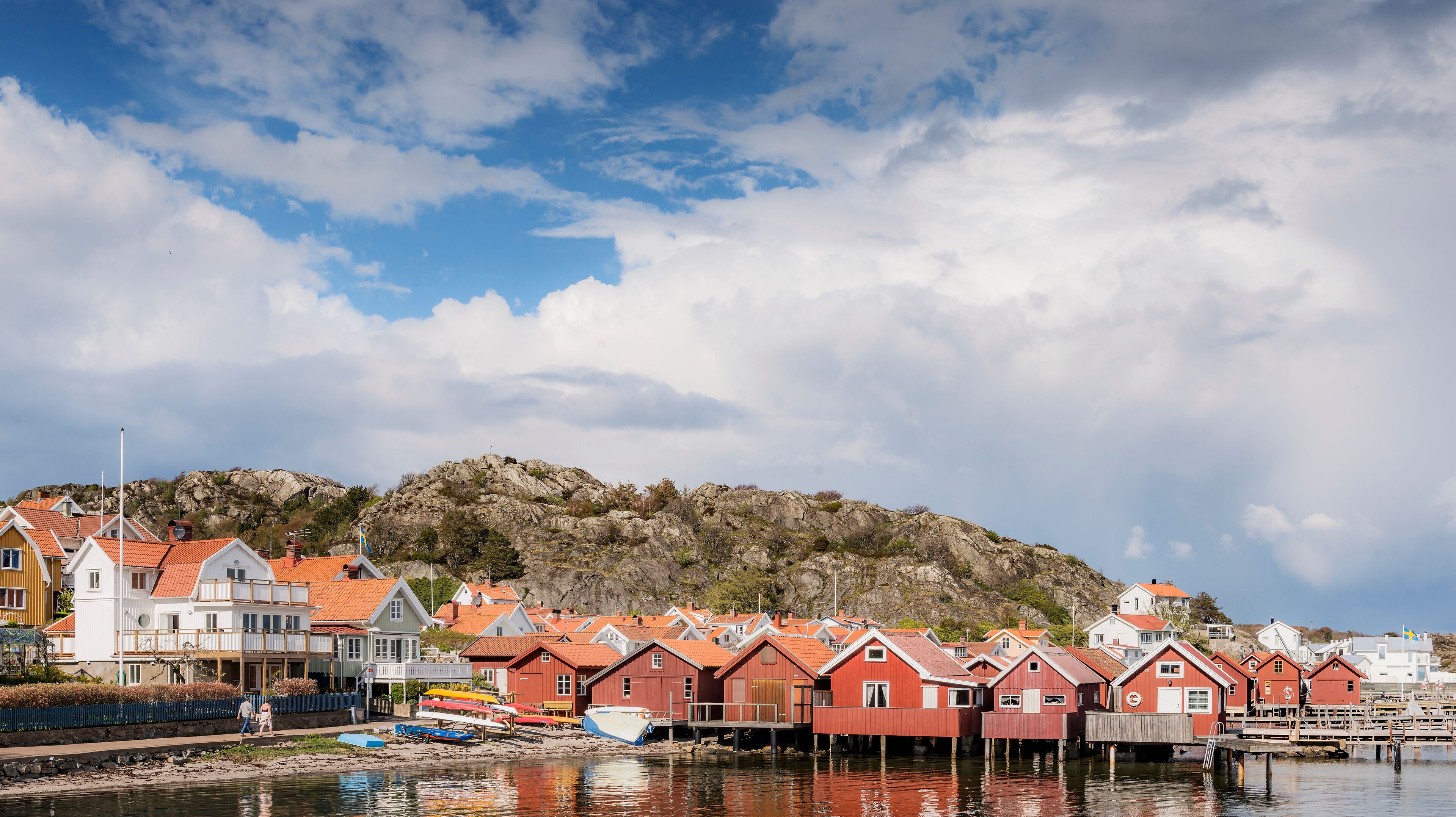 A coastal village with red-roofed houses and a rocky hill in the background.