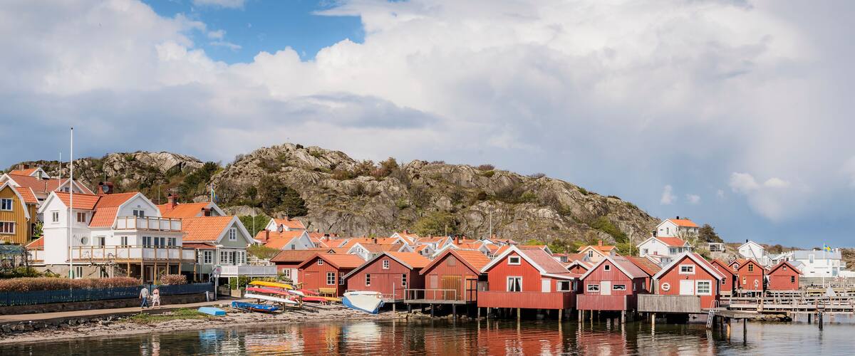 A coastal village with red-roofed houses and a rocky hill in the background.