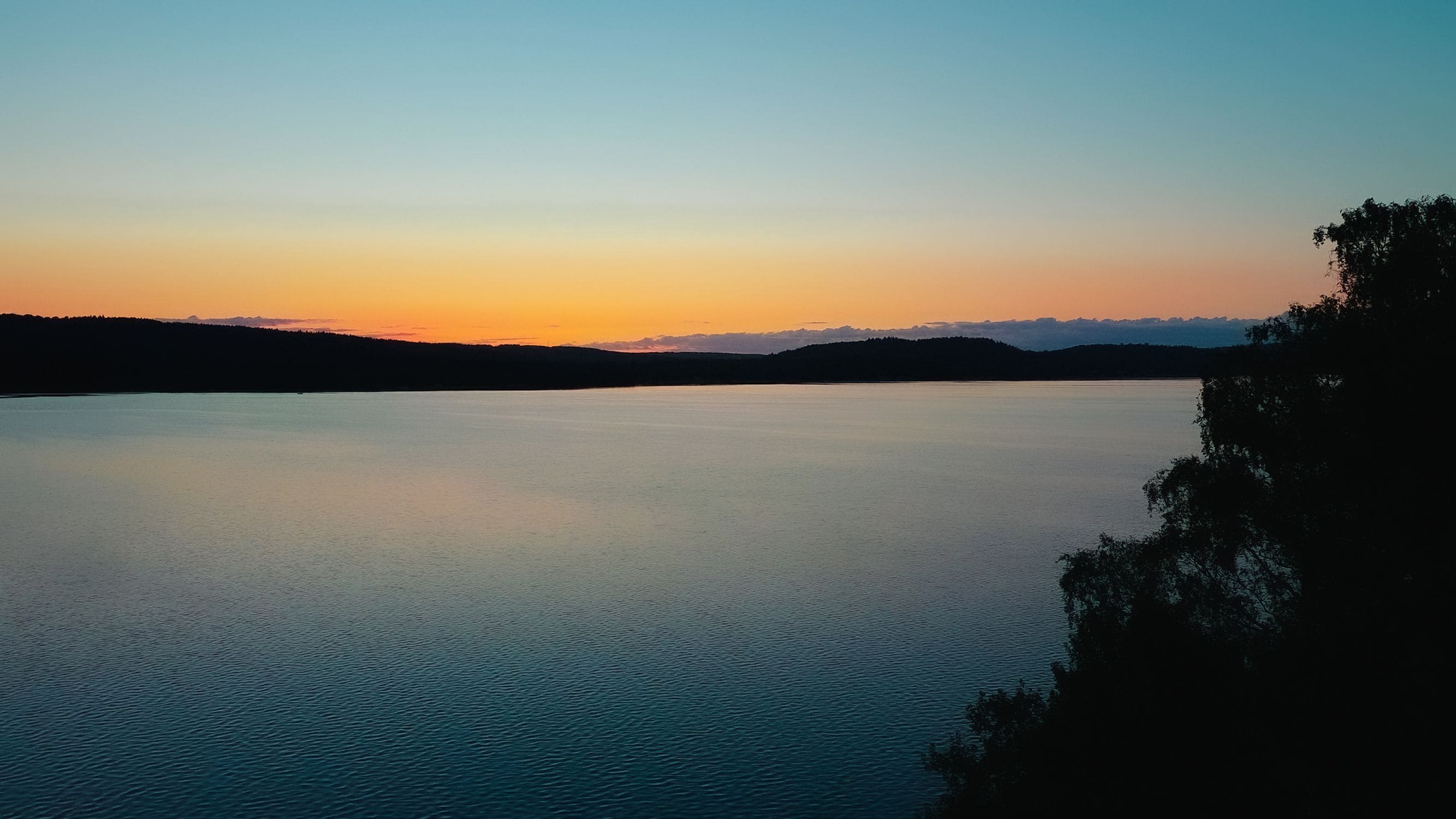 Un lago tranquilo al atardecer, con cielo despejado y montañas distantes.