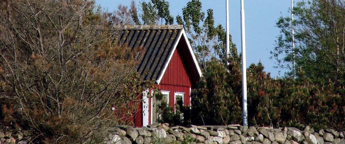A red barn with a Swedish flag on a flagpole, surrounded by trees and a stone wall.