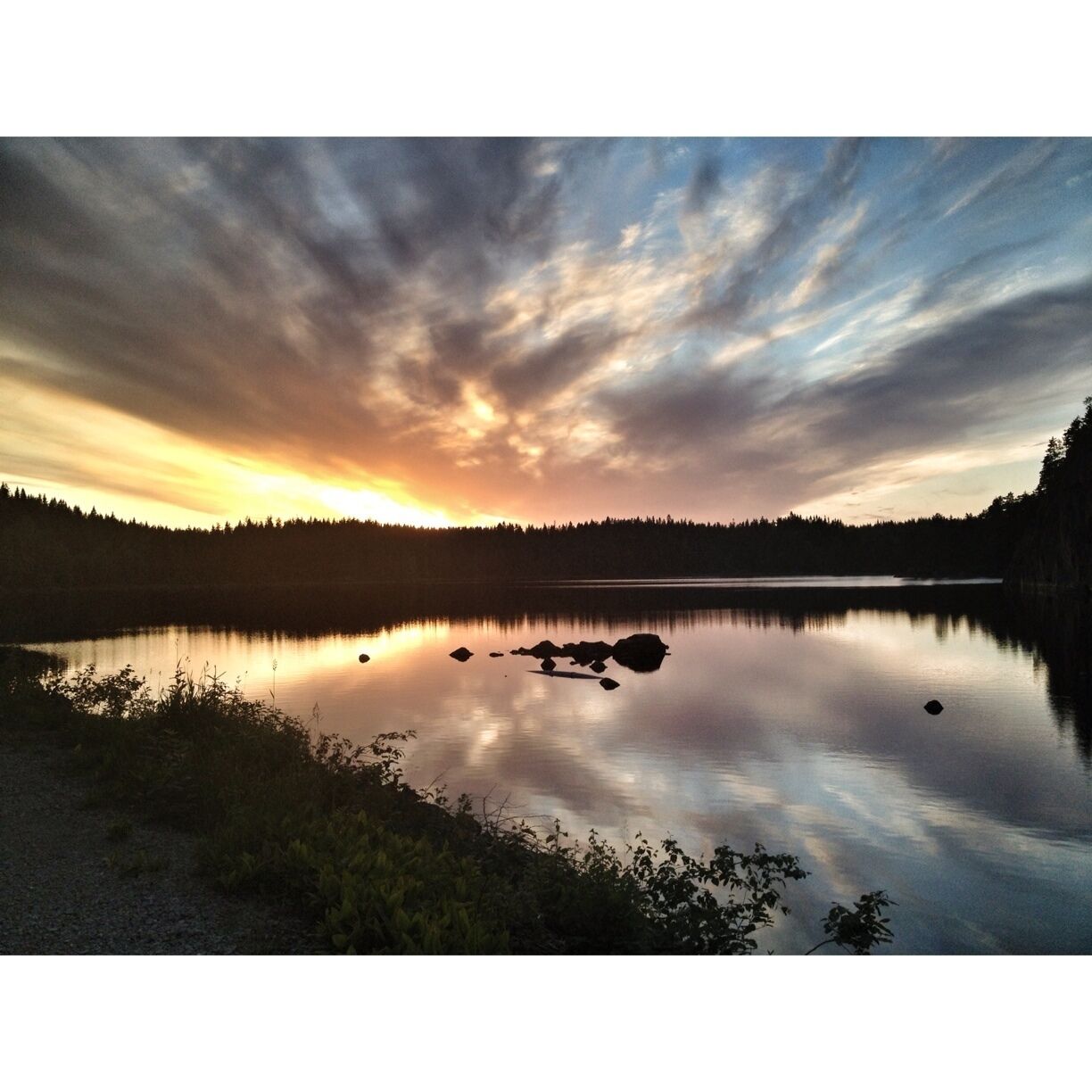 A calm lake at sunset with a forested shoreline and a clear sky.