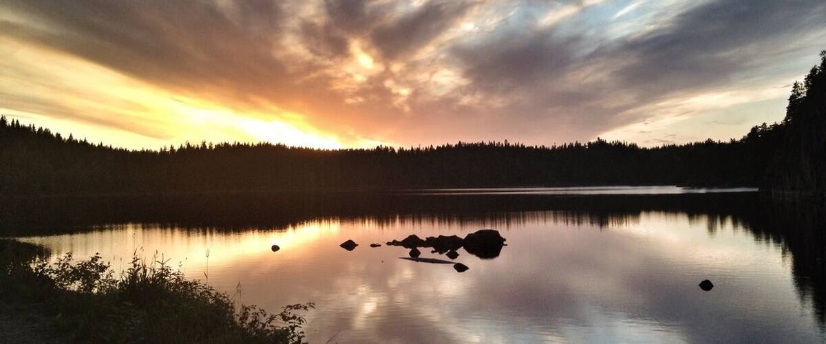 A calm lake at sunset with a forested shoreline and a clear sky.